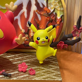 Yellow Pikachu toy with a red creature and pink flowers on a textured surface